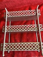 Front view of the vintage 3-tier metal rack showing the cream-colored lattice sides and metal trays on red background.