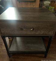 Photo showing the front view of the side table, highlighting the wooden top surface, drawer with metal handle, and bottom shelf with black iron rod frame.