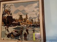 Framed embroidery of skating on a canal in Holland with windmill, buildings, and people skating on frozen canal.
