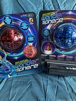 Two new Wonder Sphere magic hover balls in red and blue packaging, displayed in blister cards on a fabric surface.