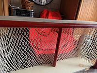 Photo showing handmade wooden hockey net trophy stand with red and white paint and mesh netting.