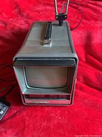 Front and side view showing the vintage Zenith black and white TV unit with integrated AM-FM clock radio and handle on top.