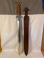 Full view of decorative sword with wood handle, brass guard and leather sheath
