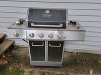 Front view of Dyna-Glo gas barbecue grill showing four control knobs, dual cabinet doors, side shelves, and handle.