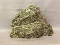 Front view of vintage hardstone sculpture depicting two abstract faces carved together in green and brown mottled stone.