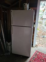 Full view of closed white Hotpoint fridge-freezer showing wear, in storage area with paint can on top.