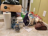 Lot containing T-Fal iron, toiletries, paper towel roll, ceramic snowman figurine, cosmetic bags, and travel pouch on countertop