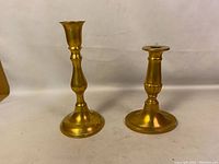Both brass candlesticks side by side on a plain background showing height and style difference
