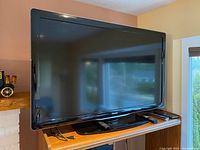 Front view of Philips 55 inch flat screen TV on wooden stand with remote controls on the base.