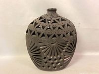 Front view of the pierced ceramic vase showing geometric cutouts and fan carving detail.