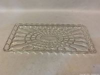 Full view of the rectangular clear pressed glass serving tray showing the intricate central flower-like geometric pattern and scalloped edge.
