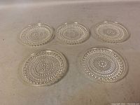 Top view of five clear glass coasters arranged in a roughly circular shape showing the textured raised dot pattern.