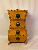 Front view of the small four-drawer dresser cabinet showing curved wooden body with metal stud accents and four dark metal knob handles on the drawers.