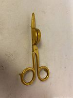 Side and profile view of the brass candle snuffer showing the scissor handles, bell-shaped snuffing cup and small feet allowing the snuffer to stand upright.