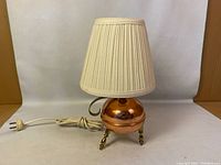 Front view of the vintage copper table lamp with cream pleated shade and attached electrical cord.