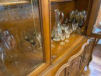 Photo of vintage crystal glassware inside wooden cabinet, showing various stemmed glasses and decanter.