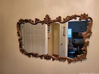 Front view of vintage wall mirror mounted on a wall, showing the ornate wood carved floral and scroll designs around the edges.