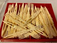 Tray of ivory-colored cocktail forks with three tines and ornate grape cluster sculptured handles.