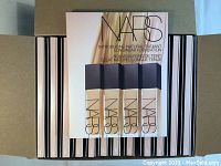 Box containing multiple sample vials of NARS Natural Radiant Longwear Foundation in medium shades and total 100ml volume, stacked in rows.