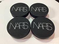 Four NARS round black lid jars seen from top with NARS logo in white.