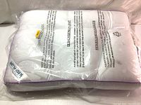 Image of pillow inside clear plastic packaging showing text warnings and folding pattern of pillow