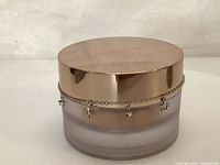 Front view of the frosted glass foundation jar with gold lid and decorative star charm chain.