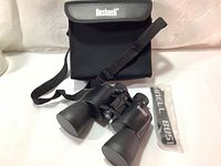 Bushnell Power View binoculars with lens covers, black soft carrying case with Bushnell logo, and unopened neck strap.
