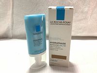 Front view of blue tube of La Roche-Posay Hydraphase Intense Riche face cream with matching box beside it on white fabric background.