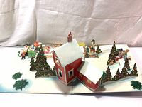 Photo of pop-up Christmas present decoration showing a red house with snow on the roof, decorated trees, and small Christmas elements.