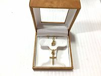 Open tan jewelry case with white padding featuring a gold tone rhodium plated crystal cross necklace and matching pendant inside.