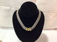 Thick metallic mesh-style necklace displayed on a black velvet stand highlighting the texture and gold-tone clasp.