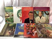 Eight Christmas-themed vinyl LP album covers displayed upright; includes artists Andy Williams, Perry Como, and others with Christmas scenes and portraits.