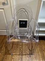 Front view of clear acrylic chair with arms and rounded backrest, showing chair shape and shadow effect on hardwood floor.