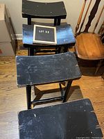 Four black wooden bar stools stacked, showing tops and wear