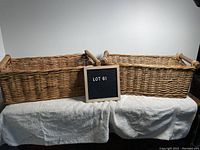 Two rectangular woven baskets placed side by side on a white towel, showing overall size and shape with a sign displaying lot number.