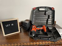 Black & Decker cordless drill in carrying case with battery charger and two battery packs, on wooden surface next to a sign 'LOT 18'.