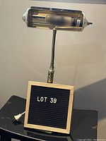 Front-side view of metal adjustable desk lamp showing bulb housing, flexible neck, and circular base with wrapped cord and plug.