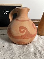 Close-up of Greek ceramic pot, beige with reddish swirl patterns, rounded body, narrow neck with handle.