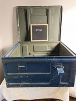 Front open view of the military style blue tin munitions box with hinged lid showing the interior in olive green and one missing latch on the front side.