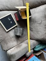 Photo showing the finishing sander with its power cord and box alongside a yellow-handled sledge hammer, placed on a couch.