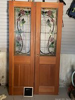 Front view of two wood-framed interior doors featuring upper stained glass panels and lower solid panels