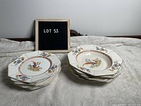 Stack of six octagonal peacock pattern bowls and six matching plates with a sign displaying 'LOT 53' in the background.