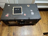 Top view of black vintage trunk lid showing wear, vintage travel-related stickers including hotels and locations.