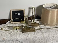 Pair of brass-coloured adjustable wall sconces with beige lampshades, placed on a white cloth background with a lot number sign.