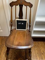 Front view of the wooden chair showing contoured seat, backrest with carved detail, and turned legs.