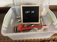 Photo of plastic bin containing various used wrenches including a large red pipe wrench, several open-end and combination wrenches, a yellow screwdriver, and a plastic bag with an unknown item.