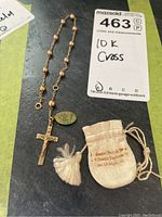 Photo showing the entire lot: gold crucifix and prayer beads, Mary charm, and small beige leather pouch on black background.
