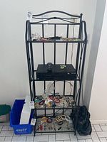 Full view of black metal bakers rack, showing four glass shelves and decorative curved top frame. The rack is empty in this listing; contents on shelves not included.