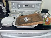 Lot displayed on stove showing Corning Ware casserole with glass lid, glass butter dish, baking pan in wicker holder, cookie jar, and salt and pepper shakers.