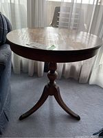 Side view of round wooden claw foot side table near a sofa, showing overall shape and condition.